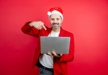 Man in santa hat smiling, holding a laptop, and pointing, celebrating a winter holiday