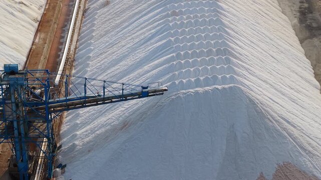 Industrial salt production site near Santa Pola, Spain, with white salt piles and blue conveyor structure by the coast.