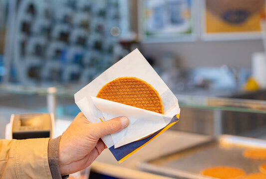 Tourist hand holding Traditional Dutch fresh made Stroopwafel, Street food treat made from thin, crispy waffles filled with rich caramel syrup, freshly prepared at local markets in The Netherlands. 
