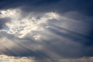 Bright columns of sun rays pass through grey overcast clouds. Holy Light comes from heaven on Earth. Visible sunbeams pillars in sky