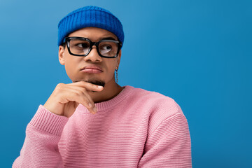 Charming young man showcases unique style with thoughtful expression in vibrant setting