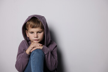Upset little boy near light grey wall indoors, space for text