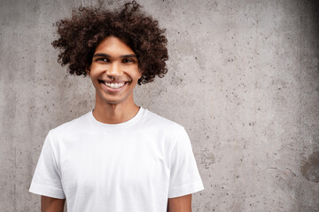 Young man with curly hair smiling standing against concrete wall