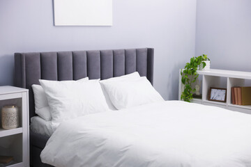 Large bed with linens, shelving unit and cabinet near grey wall in bedroom