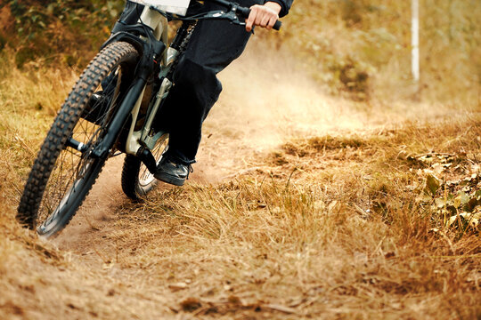 Mountain biker turning quickly on dry forest trail during downhill race. Dust and motion blur show power, control and adrenaline. Extreme sport concept.