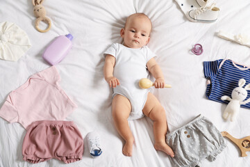 Cute baby, different clothes and accessories on bed, top view