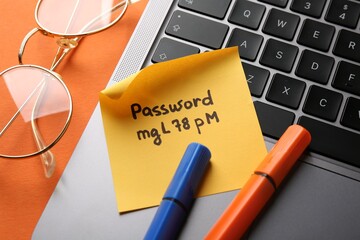 Paper note with password, markers, glasses and laptop on orange background, above view