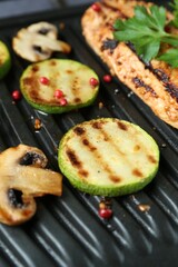 Tasty mushrooms, spices, zucchini and chicken fillet on black electric grill, closeup