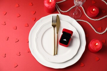 Beautiful table setting for romantic dinner and box with engagement ring on red background, flat lay