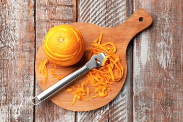 Orange zest, fresh fruit and zester tool on wooden table, top view