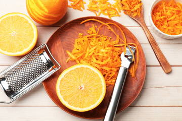 Orange zest, fresh fruits, zester tool and grater on light wooden table, flat lay