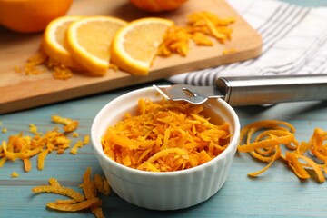 Orange zest and zester tool on light blue wooden table, closeup
