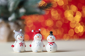 Cute decorative snowmen on white table against red background with blurred lights, closeup. Space for text