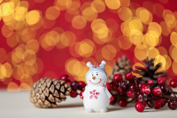 Cute ceramic snowman, cone and decorative branch with berries on white table against red background with blurred lights, closeup. Space for text