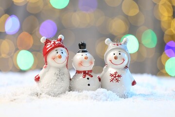 Cute decorative snowmen on artificial snow against blurred lights, closeup