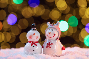Cute decorative snowmen on artificial snow against blurred lights, closeup