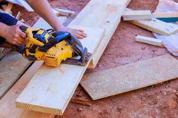 Carpenter expertly cuts long wooden planks with circular saw while working at construction site