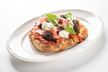 delicious oval flatbread pizza with ricotta cheese, prosciutto, spinach, and morel mushrooms on a white oval plate.