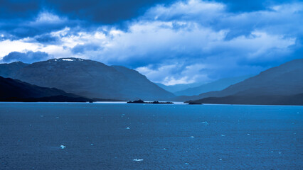 Dramatic deep blue landscape of mountains, water, and cloudy sky