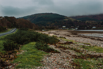 Scottish Highlands featuring a small road running through the mountains and next to a lake on an overcast autumn afternoon