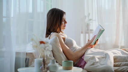 Peaceful lady flipping pages romantic novel sitting cozy bed early morning. 