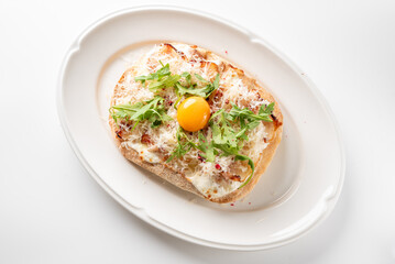 An elegant single serving pizzetta topped with creamy cheese, fresh arugula, shredded crab meat, and a bright raw egg yolk on an oval white plate on a white surface