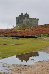 A dramatic and atmospheric photograph of the ruined medieval Castle Tioram (pronounced "Cheerum"), the former stronghold of the Clanranald branch of the MacDonalds - in Loch Moidart