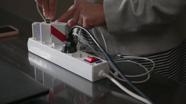Close-Up of Hands Plugging Multiple USB Charging Cables into a Power Strip for Electronic Devices