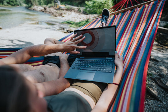 Two people working remotely from a hammock, enjoying a scenic outdoor location near water. - Powered by Adobe