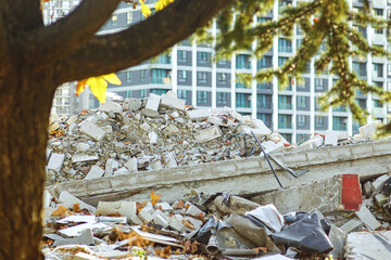 Tree-framed pile of demolished concrete with blurred modern residential buildings in the...