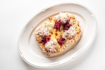 Savory toast with melted brie, red onions, and creamy sauce, topped with shredded meat or cheese. A gourmet appetizer or meal on a white plate.
