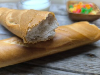 tasty pieces of baguette lie on a wooden table next to a cup of milk and candied fruits