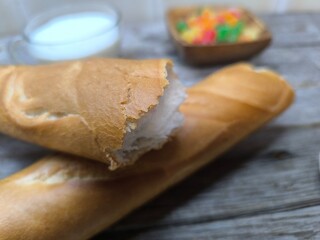 tasty pieces of baguette lie on a wooden table next to a cup of milk and candied fruits