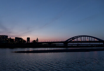 City bridge at twilight over calm river, evening lights and skyline silhouette, Japan/夕暮れに照らされた都市の橋と静かな川の風景