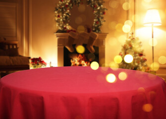 Empty table with red tablecloth in room decorated for Christmas, bokeh lights. Space for design