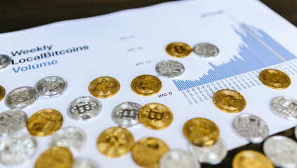 Golden and silver bitcoin coins scattered across financial report charts showing cryptocurrency market analysis and trading volume trends