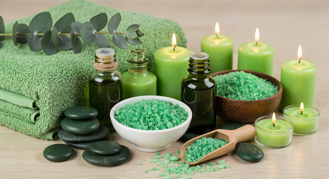 Spa essentials with green candles, oils, and bath salts on wooden surface  