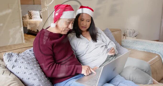 Senior couple wearing Santa hats, unfolding laptop and tapping keyboard, browsing holiday shopping