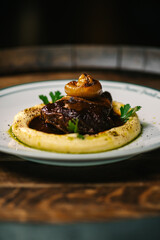 Braised beef with caramelized onion served on creamy mashed potatoes and rich brown sauce. Gourmet restaurant presentation on white plate.