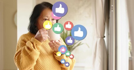 Senior woman sipping mug causing social media like icons rising past face near window reflecting - Powered by Adobe