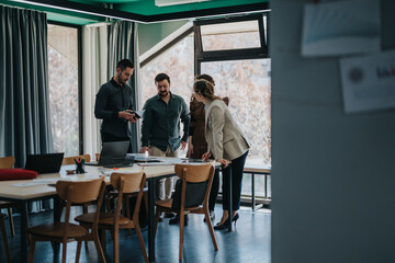 A group of colleagues discusses ideas in a contemporary office with natural lighting and laptops on the table, showcasing a collaborative work environment.