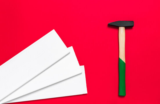 Hammer and white planks on a red background with place for text. Shop banner with construction tools, materials and instrument. New Year or Christmas holiday backdrop. Business card. Nobody.