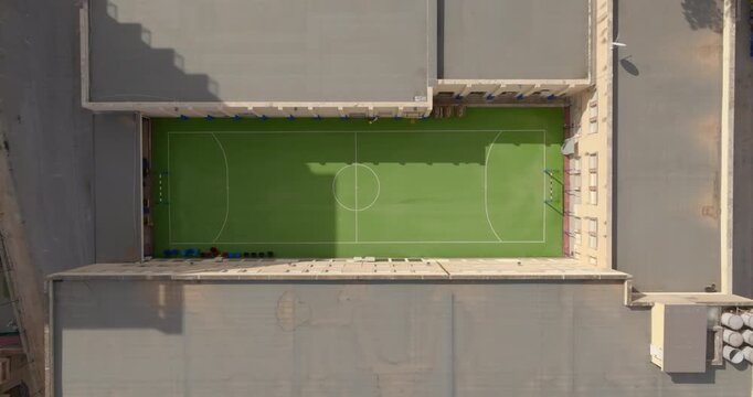Perpendicular aerial view of a synthetic grass soccer field between the buildings.