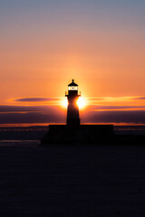 Sun Rising Behind Lighthouse Silhouette Over Calm Lake