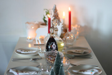 Table set for Christmas meal, with plates, wine, decorations and lit candles. Selective focus.