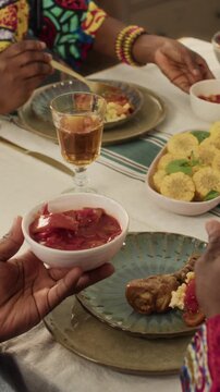 Vertical shot of unrecognisable African American man in dashiki placing letcho next to chicken drumstick on ceramic plate during Kwanzaa feast in home setting