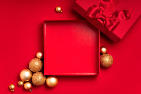 Festive red and gold flat lay with open empty box, ribbon lid and ornaments. Ample copy space for seasonal designs: Christmas and New Year banners, headers and greetings.