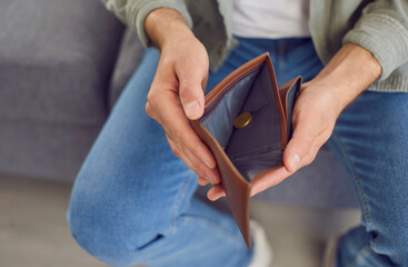 Young man opens his empty wallet with just one coin inside. Crop close up shot of hands holding a...
