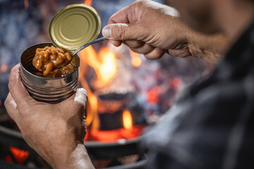 Hands holding a can of baked beans by the fire