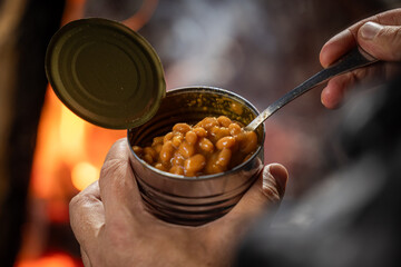Hands holding a can of baked beans by the fire